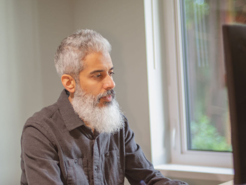 Cyrus Jagosh seated indoors by a window, looking thoughtfully to the side