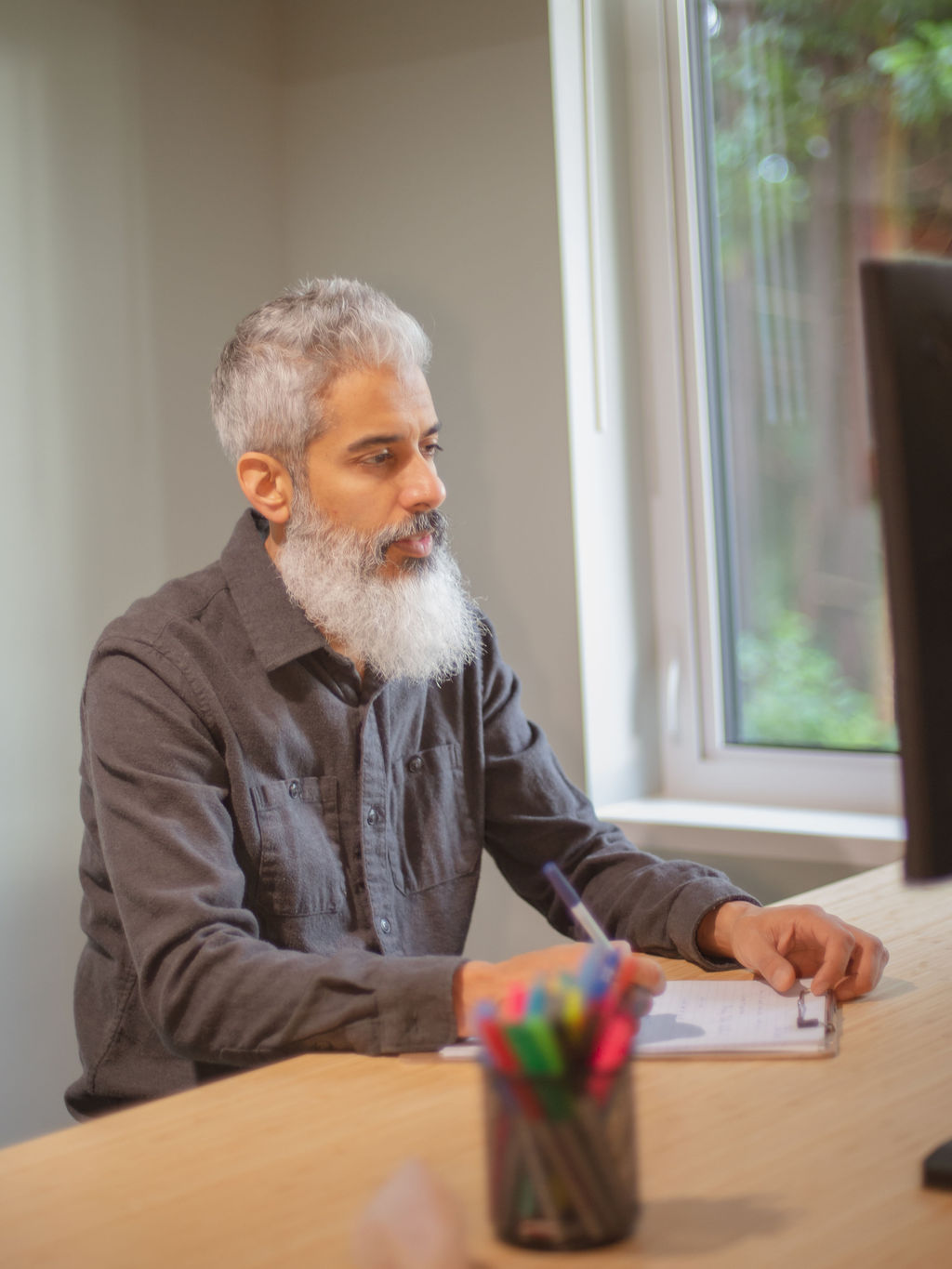 Cyrus Jagosh seated indoors by a window, looking thoughtfully at client on screen